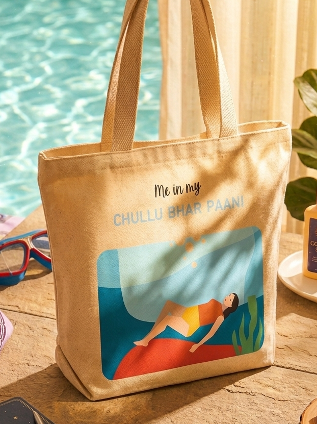 Beige tote bag with a beach scene design on a wooden table by a poolside.