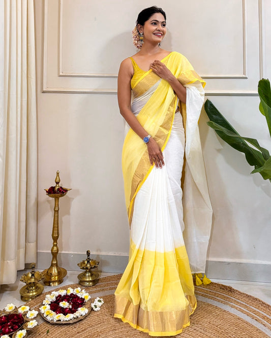 Woman in a yellow and white cotton saree standing indoors with decorative items on the floor.