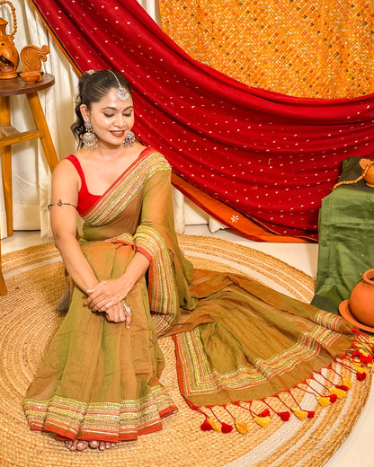 Woman in a dual tone green and red mulmul cotton saree with sequins embellished border - festive saree