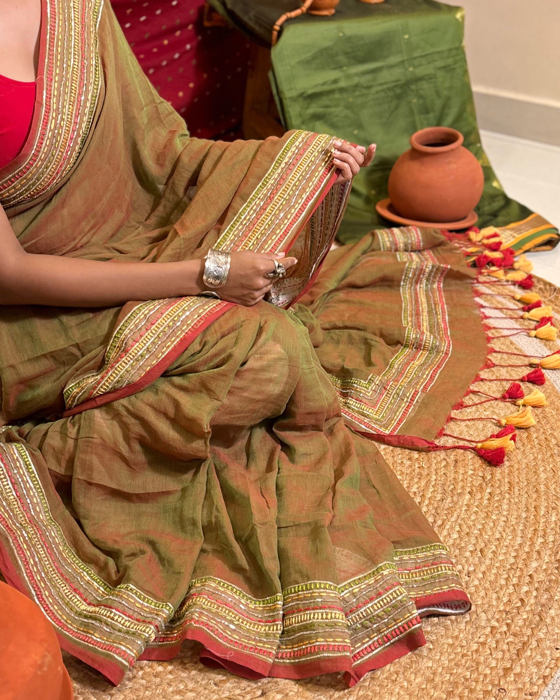 Woman in a dual tone green and red mulmul cotton saree with sequins embellished border - festive saree