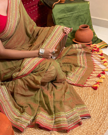 Woman in a dual tone green and red mulmul cotton saree with sequins embellished border - festive saree