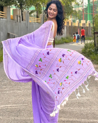 Woman in a mauve mulmul cotton  saree with floral embroidery walking outdoors.