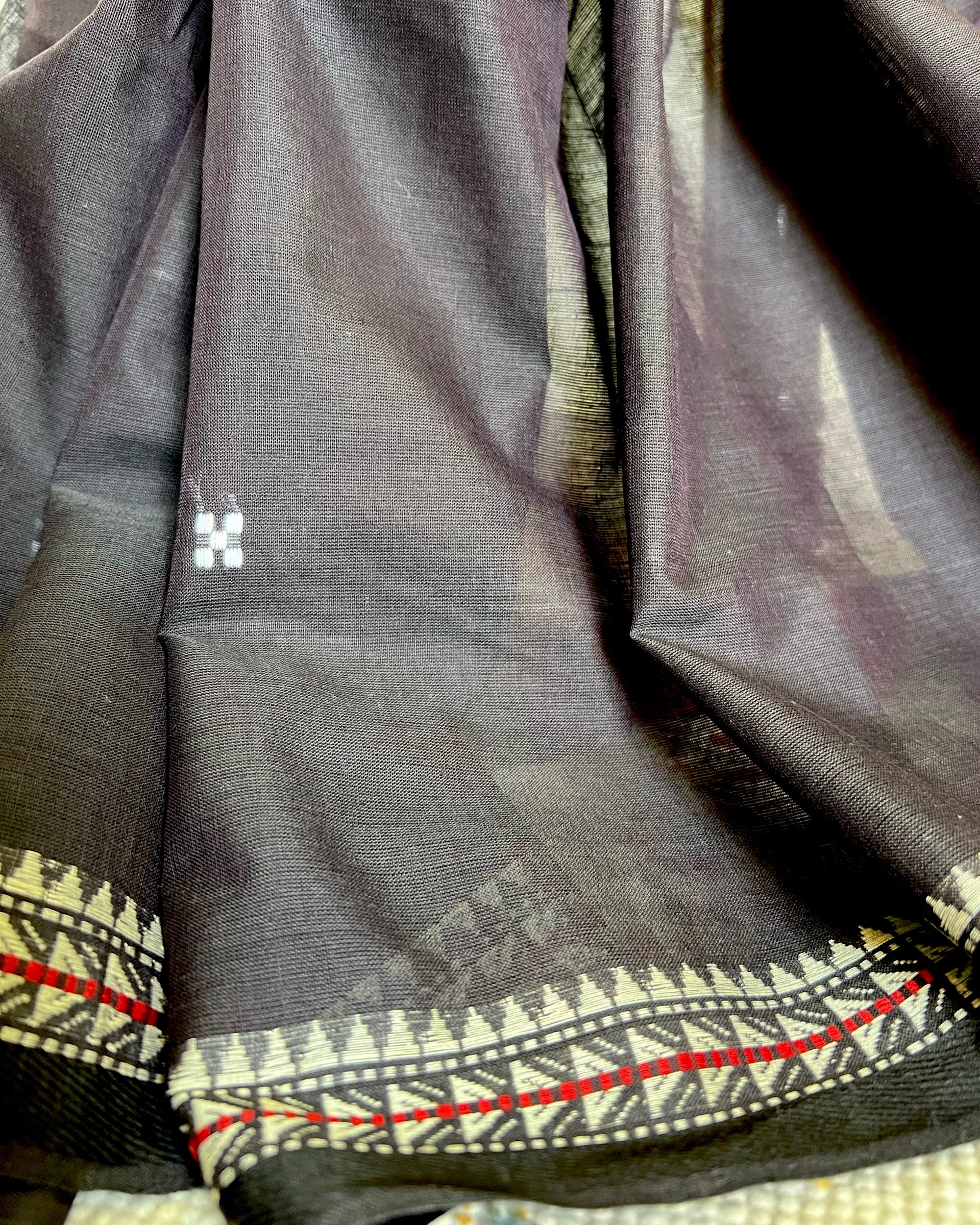 Close-up of a dark khadi cotton saree with intricate patterns and a brand logo.