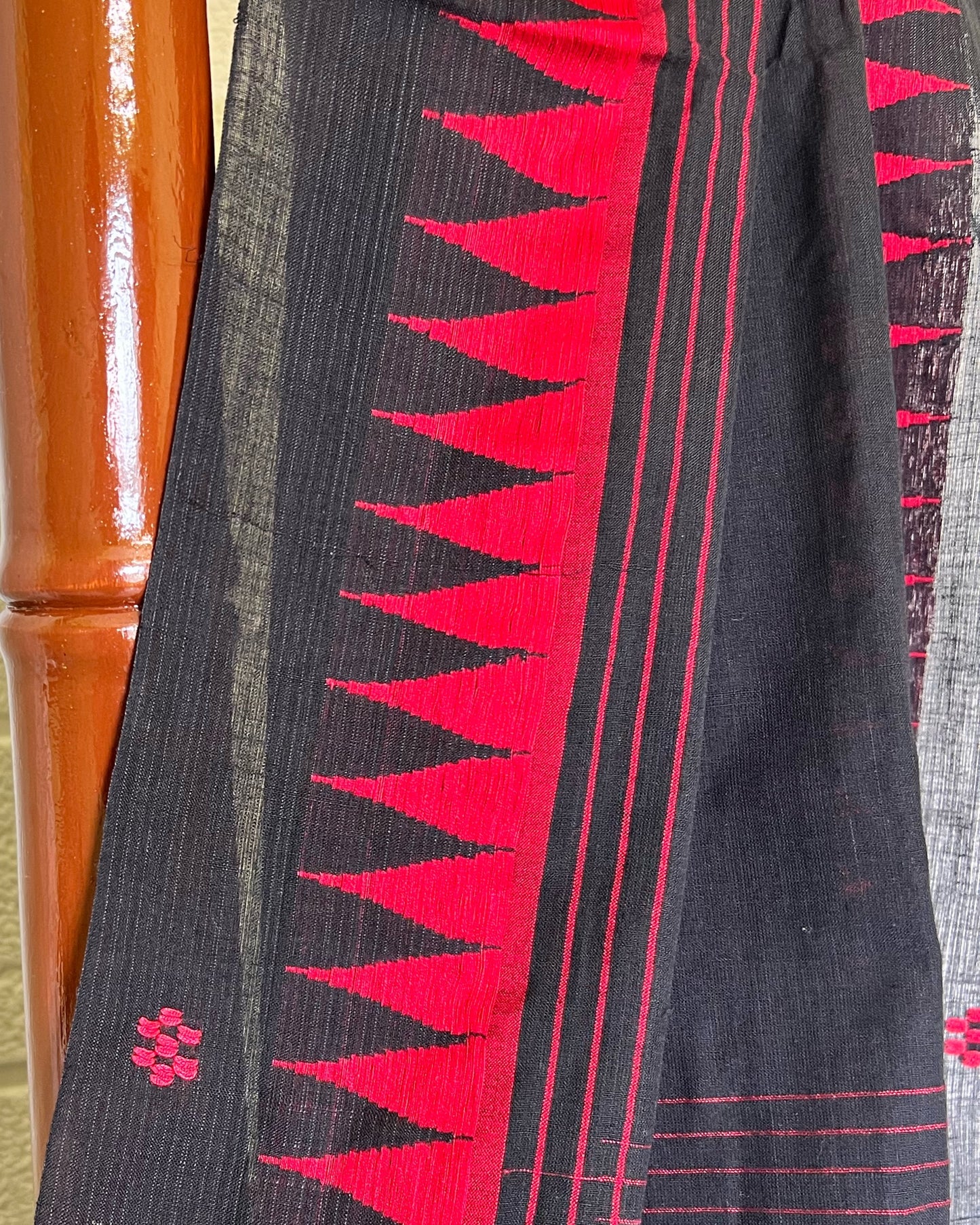 Black khadi cotton saree with red geometric pattern draped over a wooden surface