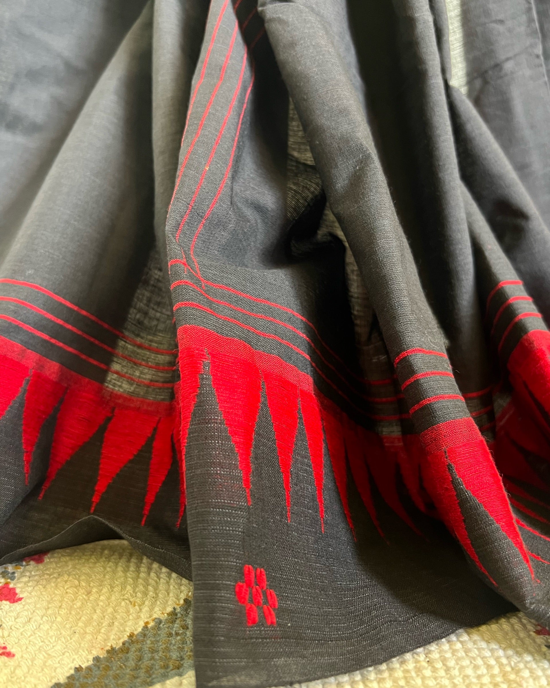 Black khadi cotton saree with red patterns and a floral design on a textured surface