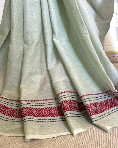 White khadi cotton saree with red and black patterned border on a beige surface