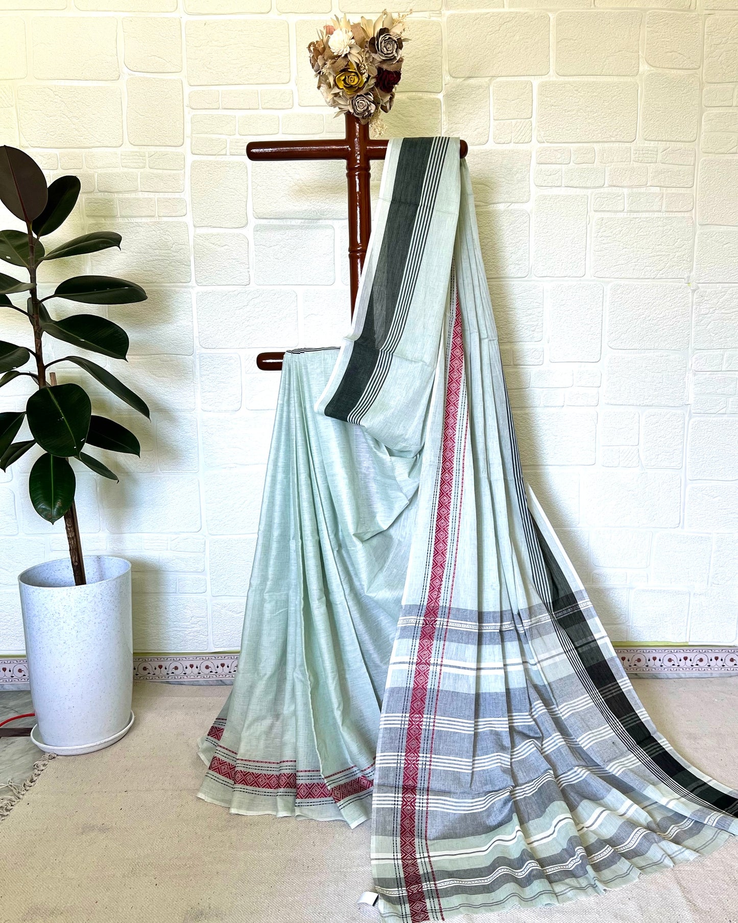 Striped khaadi cotton saree draped over a chair against a white brick wall.