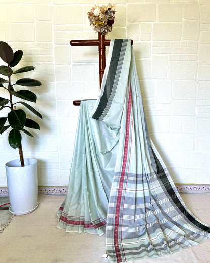 Striped khaadi cotton saree draped over a chair against a white brick wall.