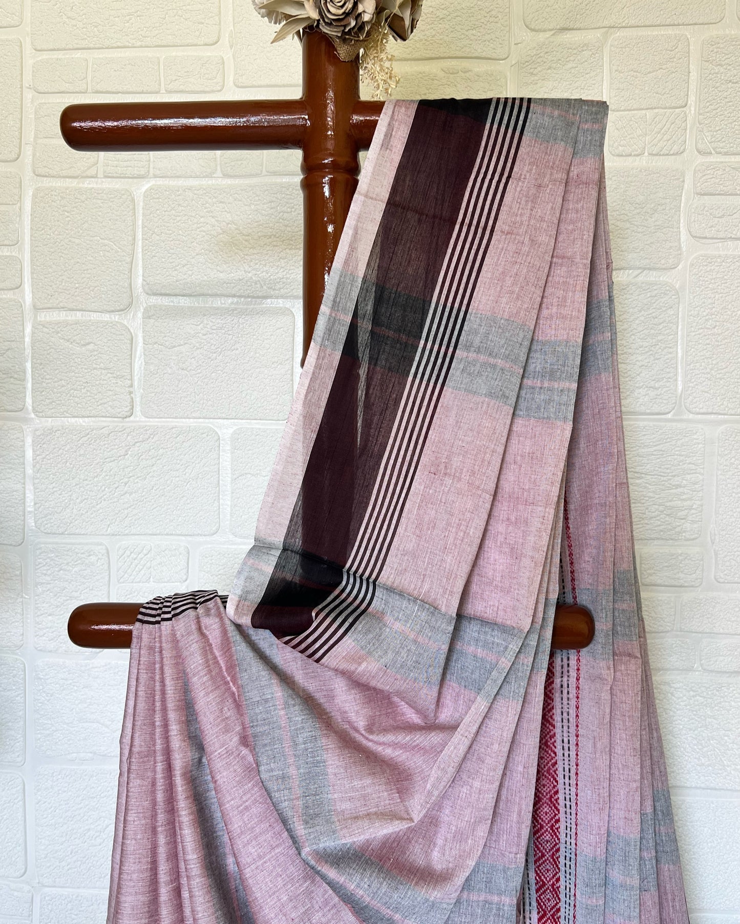 Pink and brown khadi cotton saree draped over a wooden chair against a white brick wall.