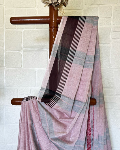 Pink and brown khadi cotton saree draped over a wooden chair against a white brick wall.