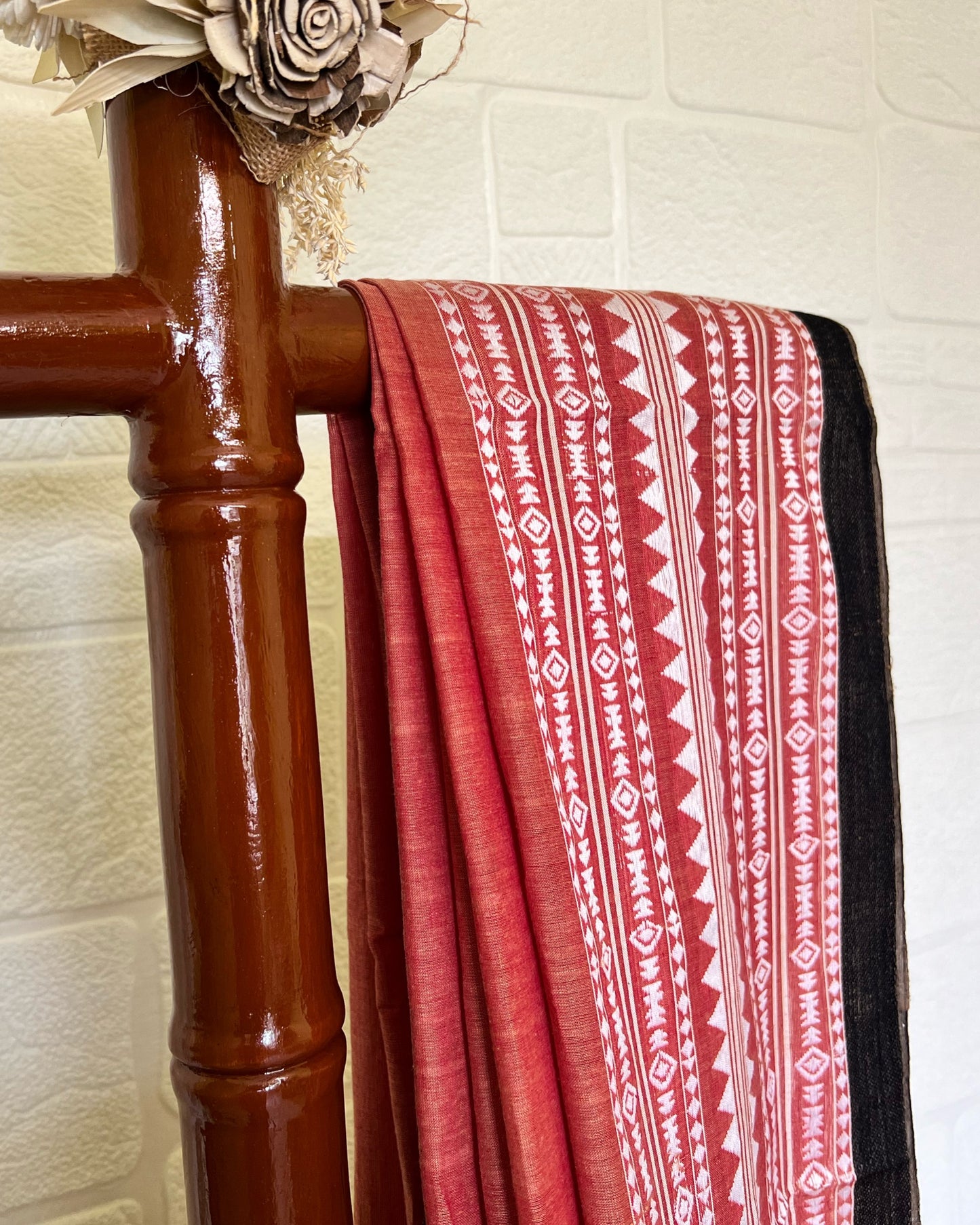 Red and white khadi cotton saree draped over a wooden rack against a light tiled wall.