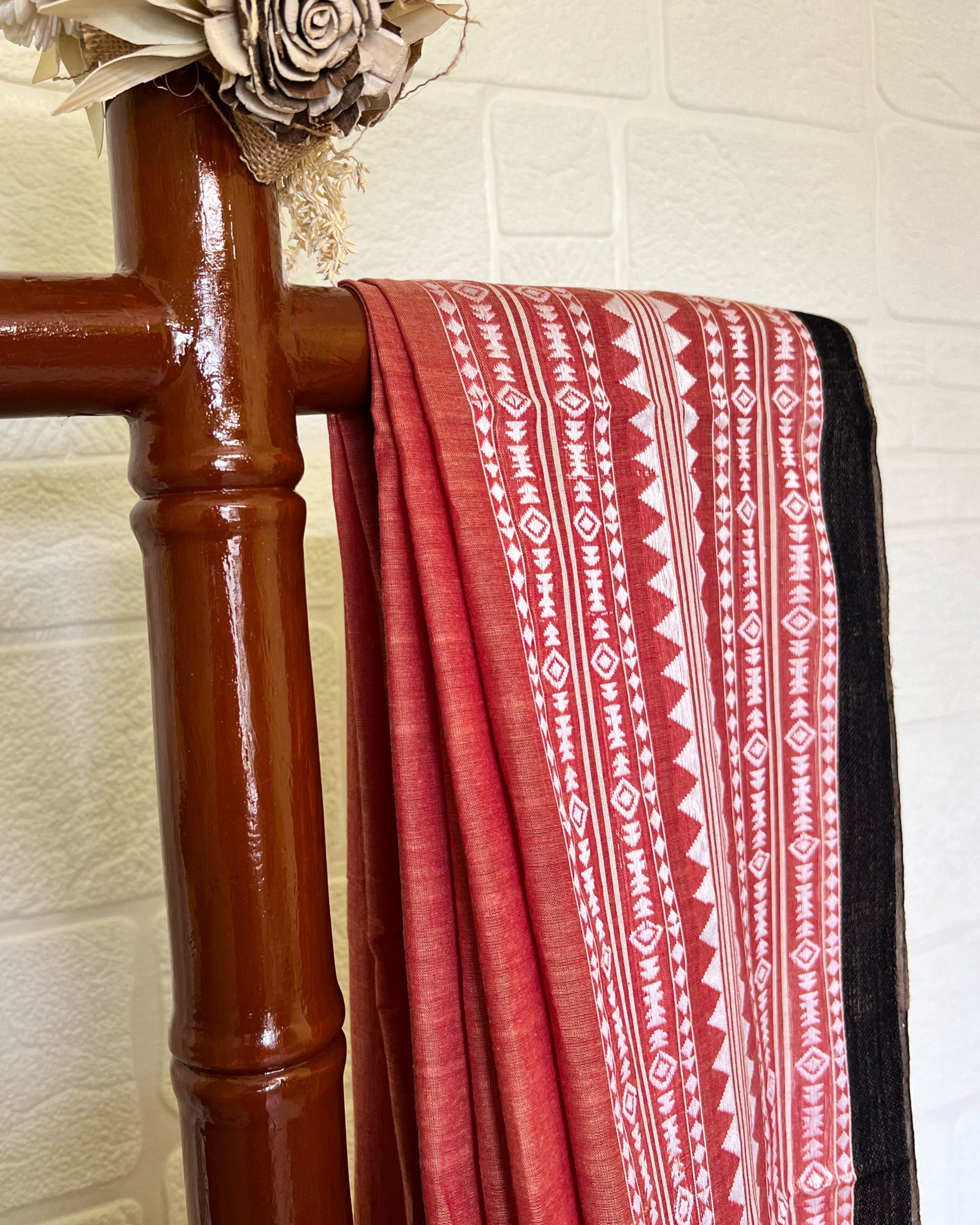 Red and white khadi cotton saree draped over a wooden rack against a light tiled wall.