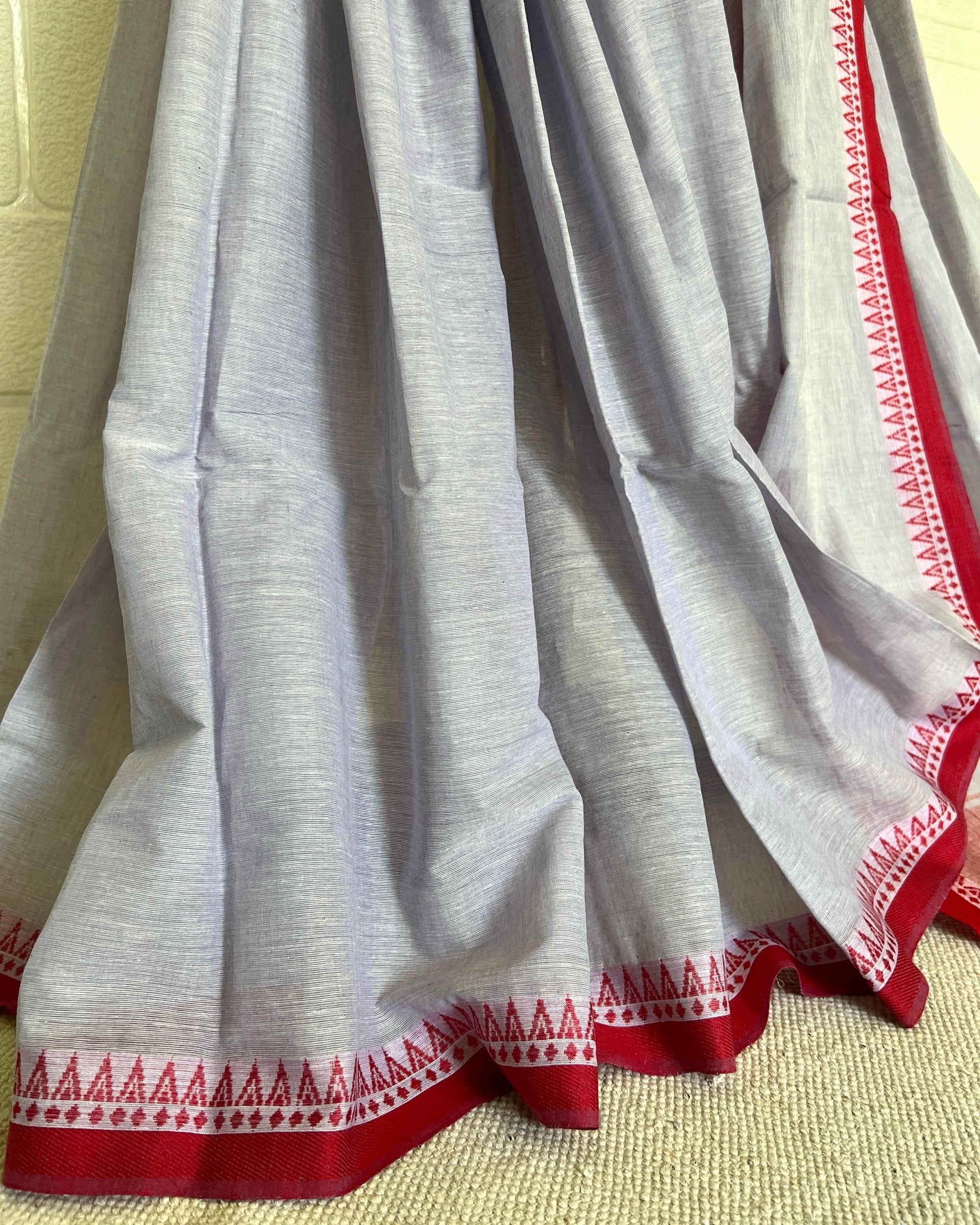 White khadi cotton saree with red and white border on a beige background