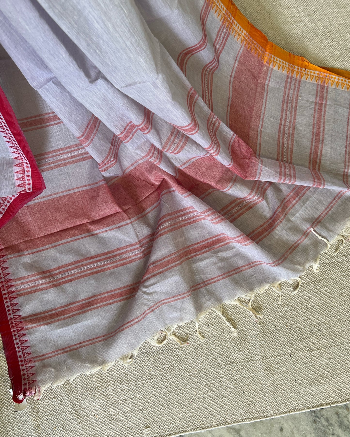 White khadi cotton saree with red stripes on a textured surface
