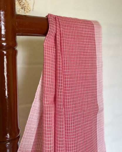 Pink checkered handloom cotton Shopaame saree draped over a wooden chair against a white wall.