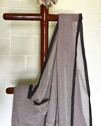 Brown checkered handloom saree by Shopaame draped over a wooden rod against a white brick wall.