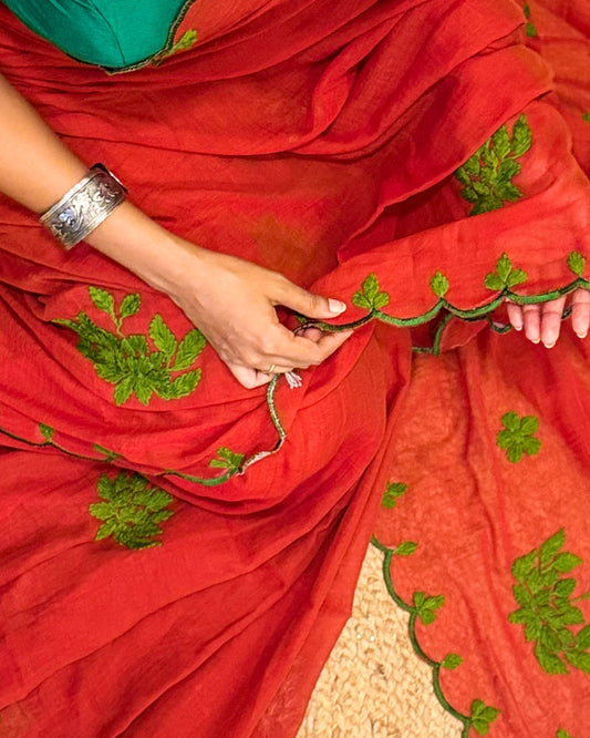 Rust Orange saree with green embroidery held by a person