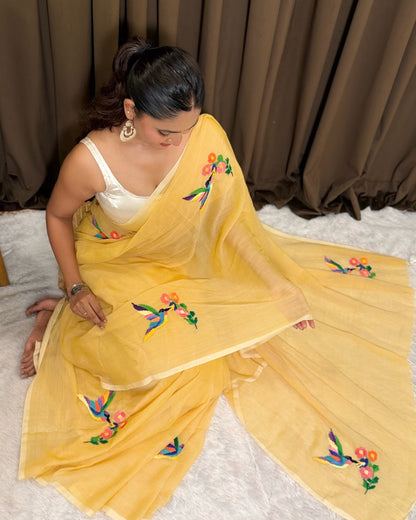 Woman wearing a yellow mulmul cotton Shopaame saree with floral embroidery against a brown curtain background