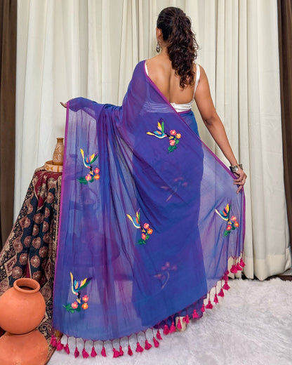 Woman wearing a purple mulmul cotton Shopaame saree with floral patterns and pink tassels in a room setting.
